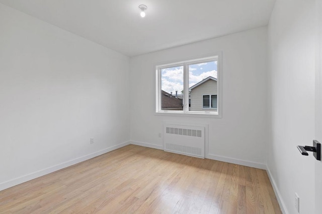 unfurnished room featuring radiator heating unit, light wood finished floors, and baseboards