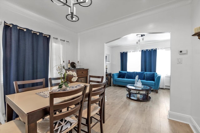 dining area with ornamental molding, light wood-type flooring, arched walkways, baseboard heating, and baseboards