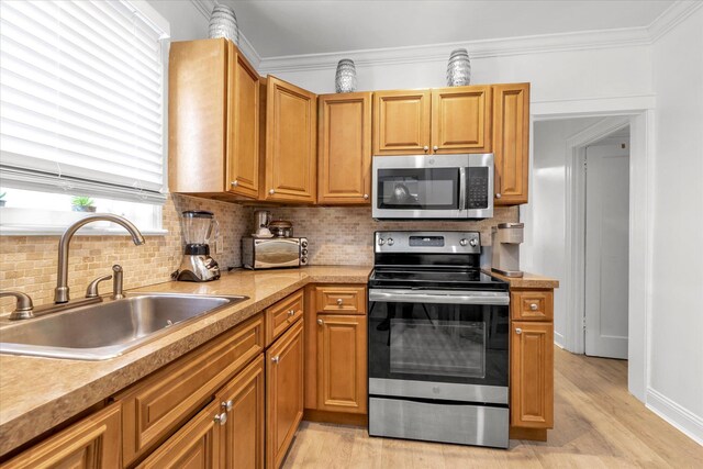 kitchen with appliances with stainless steel finishes, a sink, decorative backsplash, light wood-type flooring, and crown molding