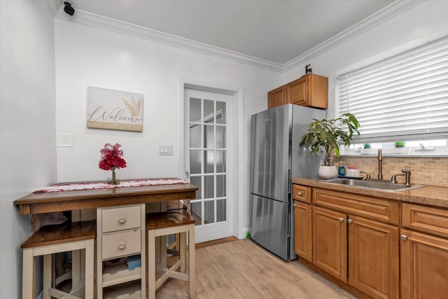 kitchen featuring a sink, freestanding refrigerator, crown molding, light wood-style floors, and brown cabinetry