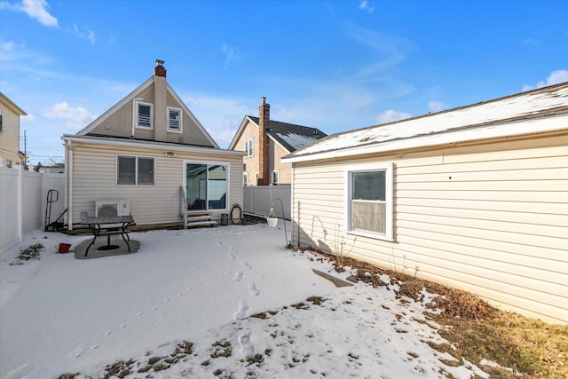 snow covered rear of property with fence, entry steps, and a chimney