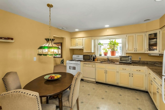kitchen featuring white appliances, under cabinet range hood, a sink, decorative light fixtures, and dark stone countertops