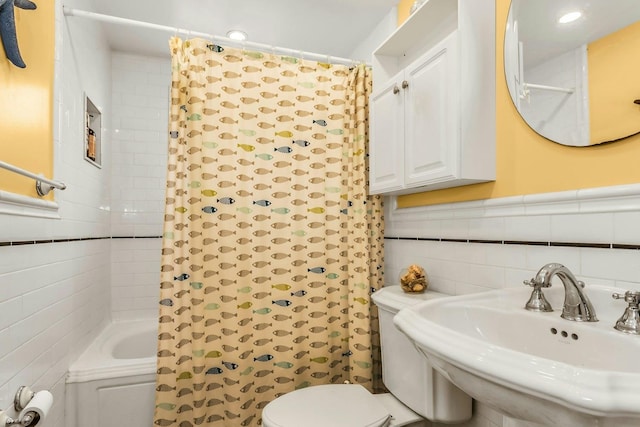bathroom with tile walls, a sink, toilet, shower / bath combo with shower curtain, and wainscoting