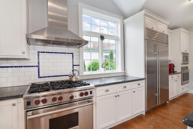 953 Peace St, Pelham, NY 10803 - kitchen with wall chimney range hood, built in appliances, healthy amount of natural light, vaulted ceiling, and white cabinets