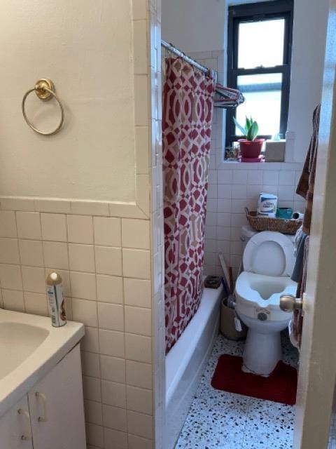 bathroom featuring tile walls, toilet, vanity, shower / bathtub combination with curtain, and wainscoting