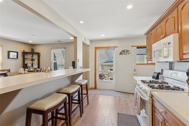 kitchen featuring white appliances, a kitchen bar, light countertops, light wood-type flooring, and recessed lighting