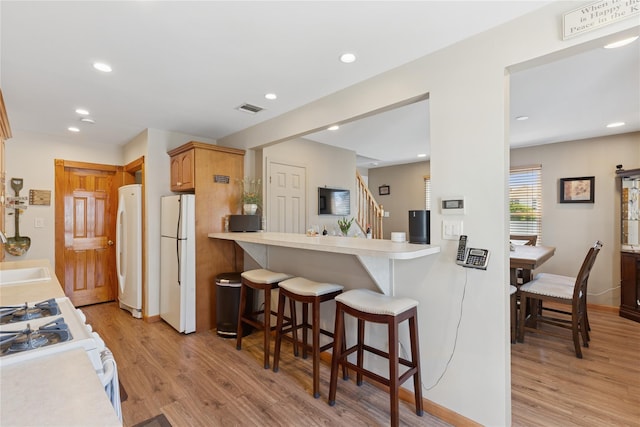 kitchen with white appliances, light wood-type flooring, a breakfast bar area, light countertops, and recessed lighting