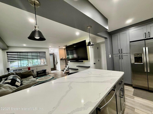kitchen featuring appliances with stainless steel finishes, open floor plan, light wood-type flooring, pendant lighting, and light stone counters