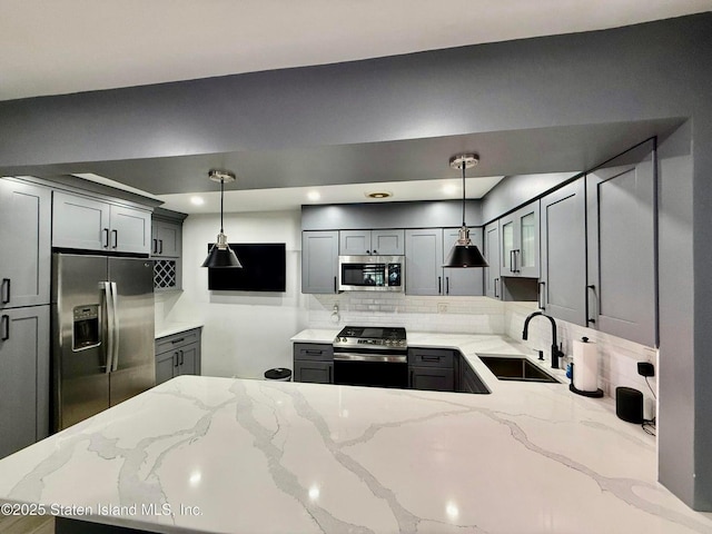 kitchen featuring appliances with stainless steel finishes, a sink, backsplash, light stone countertops, and gray cabinetry