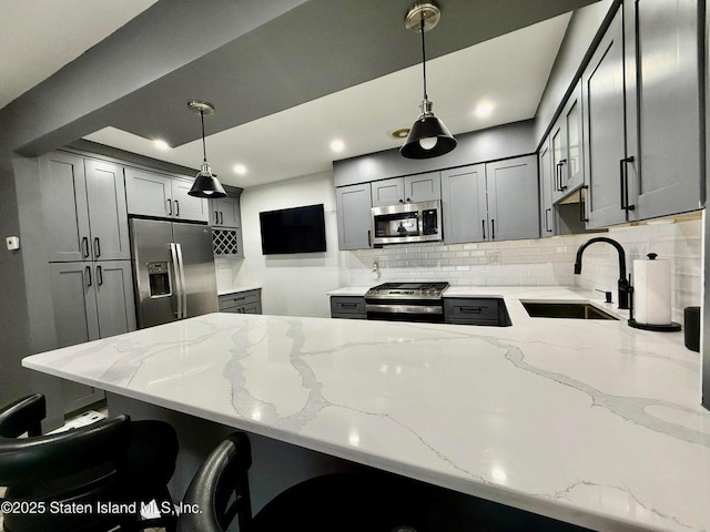 kitchen with stainless steel appliances, a sink, a peninsula, backsplash, and light stone counters