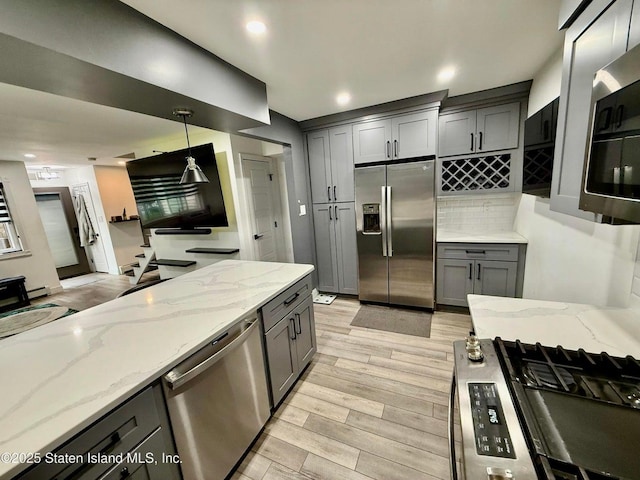 kitchen featuring stainless steel appliances, gray cabinetry, light stone counters, light wood finished floors, and decorative backsplash