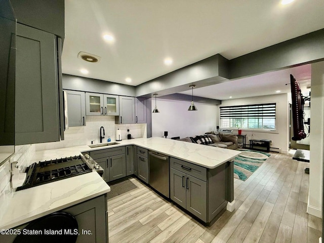 kitchen featuring stainless steel dishwasher, a sink, a peninsula, open floor plan, and gray cabinets