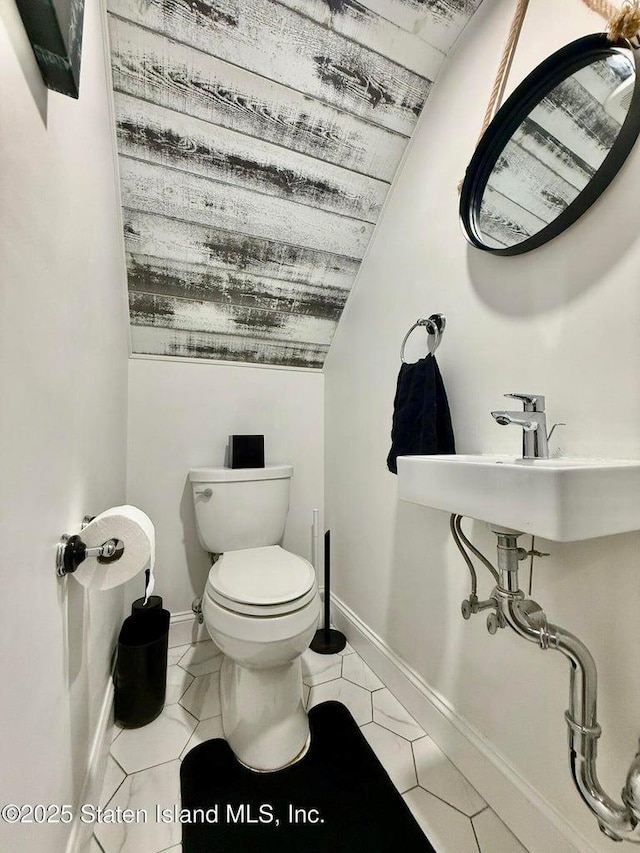 half bath with toilet, vaulted ceiling, baseboards, and a sink