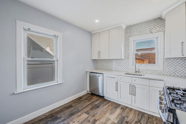 kitchen with a sink, appliances with stainless steel finishes, dark wood-style flooring, white cabinetry, and baseboards