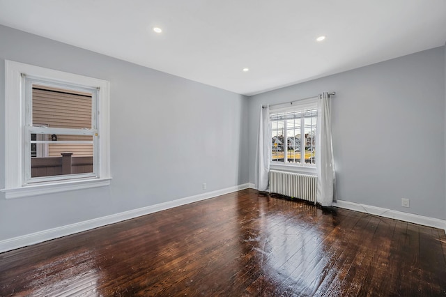 empty room featuring radiator, wood-type flooring, baseboards, and recessed lighting