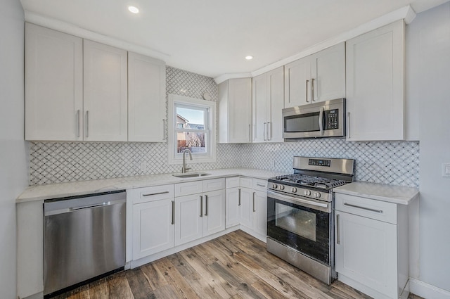 kitchen with appliances with stainless steel finishes, a sink, light wood-style flooring, tasteful backsplash, and recessed lighting