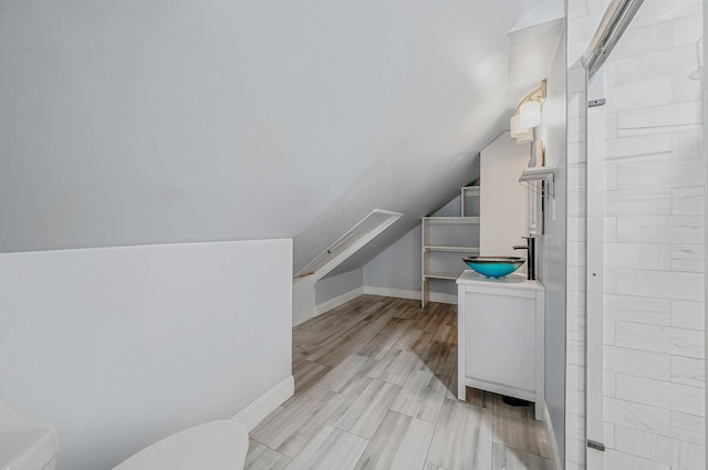 bathroom featuring toilet, vanity, vaulted ceiling, a tile shower, and wood finished floors