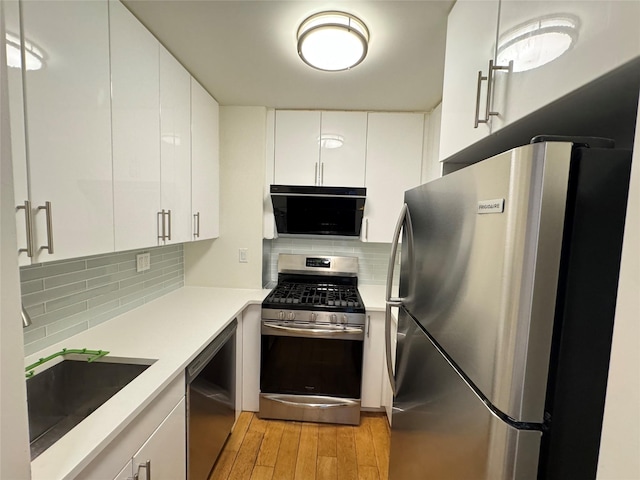 142-20 Franklin Ave Unit 2V, Flushing, NY 11355 - kitchen with stainless steel appliances, a sink, light wood-style flooring, white cabinets, and decorative backsplash