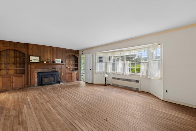 1015 Knollwood Ln, Mattituck, NY 11952 - unfurnished living room featuring radiator, light wood-style floors, a fireplace, wooden walls, and built in shelves