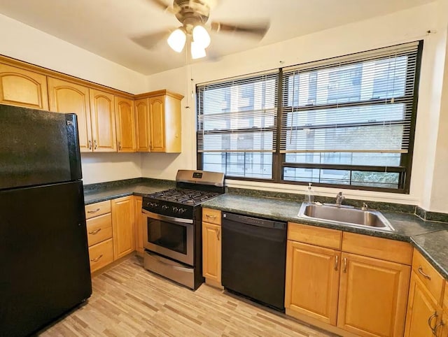 kitchen featuring black appliances, a sink, light wood-style flooring, a ceiling fan, and dark countertops