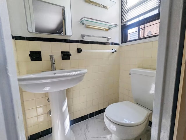 bathroom with tile walls, marble finish floors, toilet, and a wainscoted wall