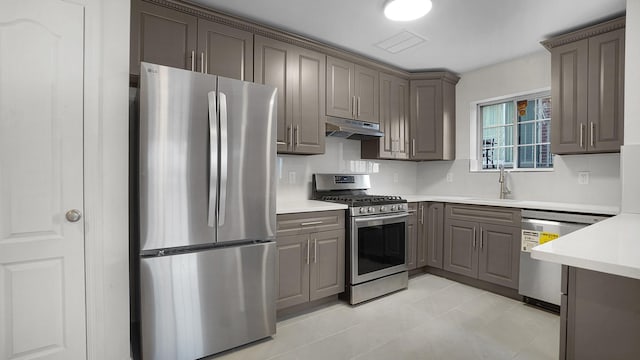 907 Clarence Ave, Bronx, NY 10465 - kitchen with stainless steel appliances, a sink, under cabinet range hood, gray cabinetry, and light countertops