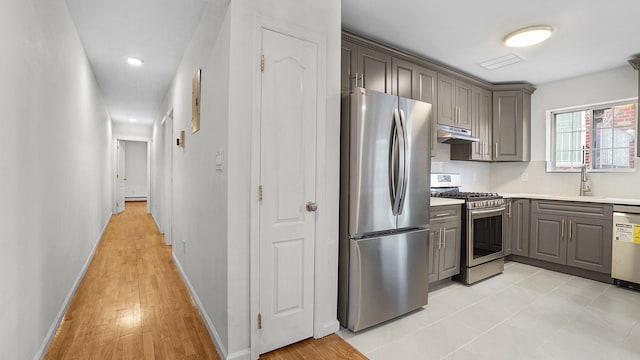 907 Clarence Ave, Bronx, NY 10465 - kitchen with stainless steel appliances, gray cabinetry, a sink, under cabinet range hood, and light countertops
