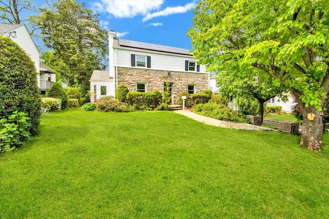 6 Mcbride Ave, White Plains, NY 10603 - view of front facade featuring stone siding, a front yard, roof mounted solar panels, and a chimney