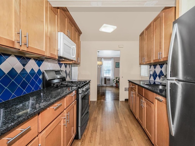kitchen with stainless steel appliances, light wood-style floors, tasteful backsplash, and dark stone countertops
