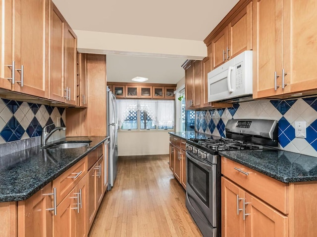 kitchen with appliances with stainless steel finishes, light wood-style floors, a sink, tasteful backsplash, and dark stone countertops