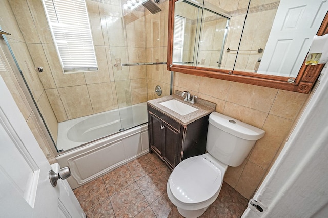 full bath with tile walls, toilet, bath / shower combo with glass door, and vanity