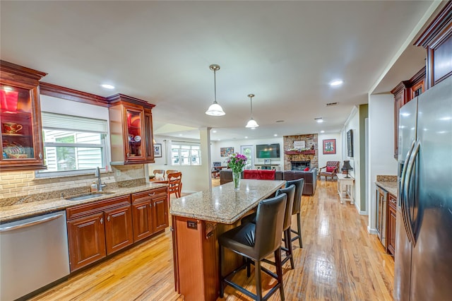kitchen featuring stainless steel appliances, a sink, light wood-type flooring, a fireplace, and a kitchen island