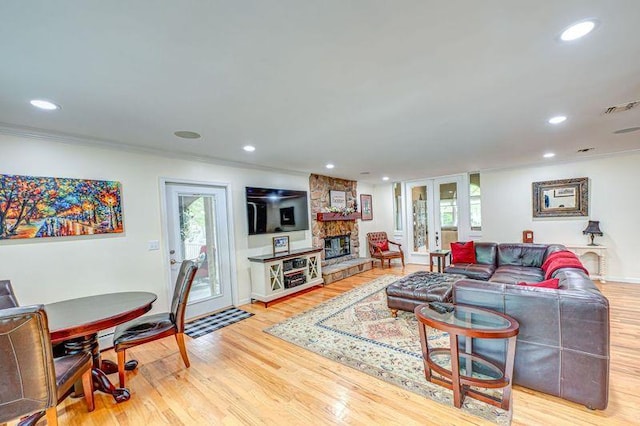 living room featuring light wood finished floors, healthy amount of natural light, ornamental molding, recessed lighting, and a stone fireplace