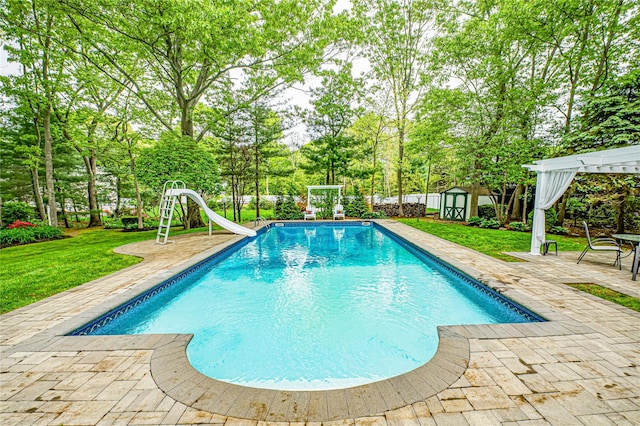 view of pool featuring a water slide, a patio area, a storage shed, an outdoor structure, and view of wooded area