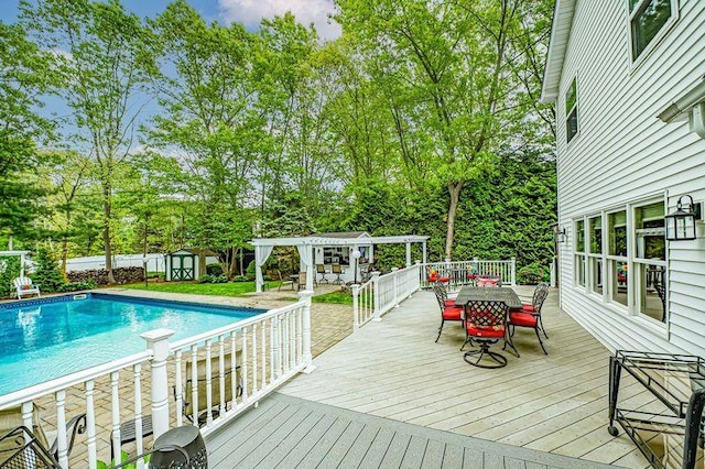 wooden terrace with outdoor dining space, a pergola, an outdoor pool, a storage unit, and an outbuilding