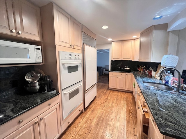 kitchen featuring white appliances, light wood finished floors, a sink, recessed lighting, and dark stone counters