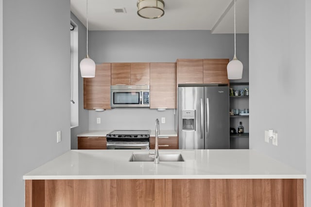 kitchen featuring appliances with stainless steel finishes, a sink, modern cabinets, decorative light fixtures, and brown cabinetry