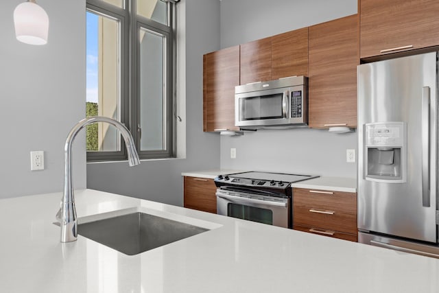 kitchen featuring appliances with stainless steel finishes, brown cabinetry, light countertops, a sink, and modern cabinets