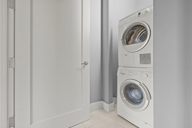 clothes washing area with stacked washer / dryer, light tile patterned flooring, and baseboards