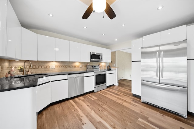 kitchen featuring stainless steel appliances, a sink, dark countertops, white cabinets, and light wood-style flooring