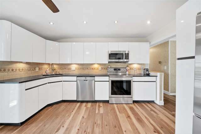 kitchen with stainless steel appliances, dark countertops, a sink, white cabinetry, and recessed lighting
