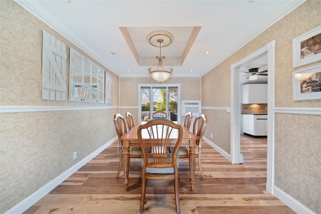 dining space featuring light wood finished floors, wallpapered walls, a raised ceiling, crown molding, and ceiling fan