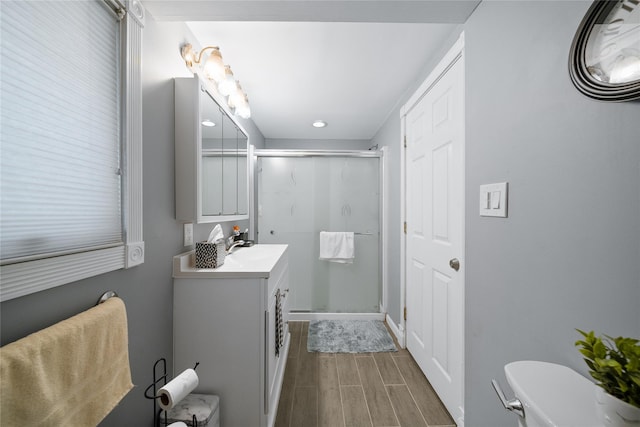 bathroom with a stall shower, wood finish floors, vanity, toilet, and recessed lighting
