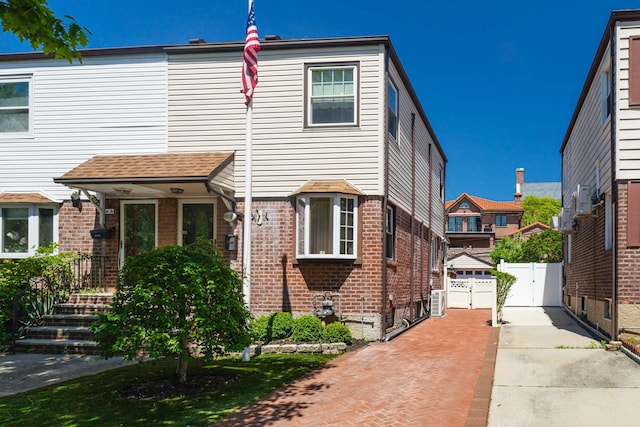 multi unit property featuring brick siding, a gate, driveway, fence, and roof with shingles