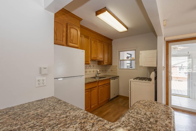 kitchen featuring freestanding refrigerator, dishwashing machine, a sink, backsplash, and healthy amount of natural light