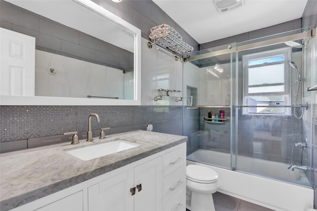 bathroom featuring toilet, vanity, bath / shower combo with glass door, tile walls, and tile patterned floors