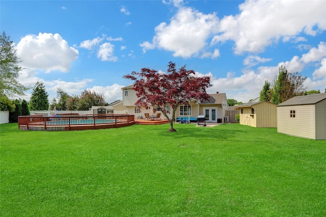 view of yard featuring a storage unit, an outdoor structure, a wooden deck, a pool, and french doors