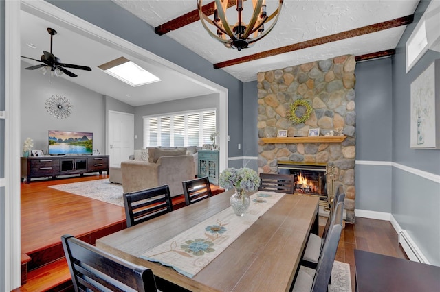 dining area with wood finished floors, a fireplace, a ceiling fan, a skylight, and a baseboard radiator