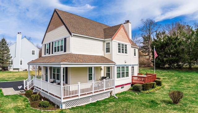 view of front of property featuring a chimney, a front yard, covered porch, and roof with shingles