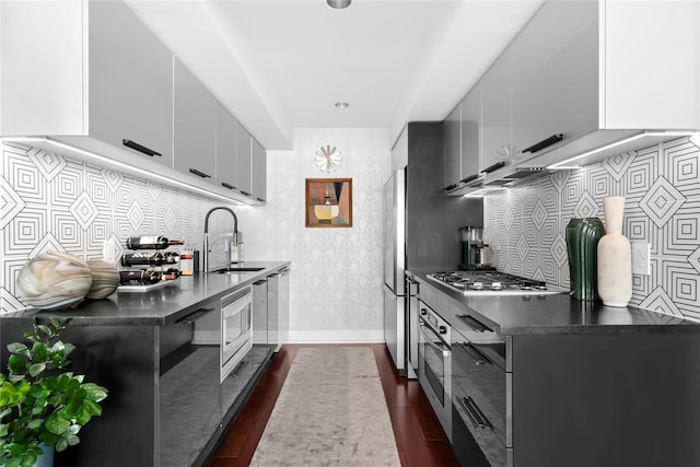 kitchen featuring a sink, stainless steel appliances, dark countertops, dark wood-type flooring, and modern cabinets